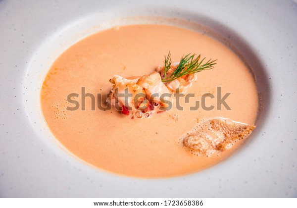 Closeup of creamy lobster bisque soup with grilled\
prawn and dill in white\
bowl