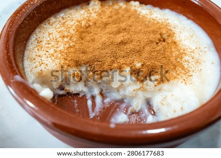 Close-up of creamy rice pudding in a rustic clay bowl, topped with a generous layer of cinnamon. Warm homemade dessert with a rich, comforting look.