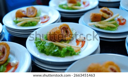 Close-up of crispy breaded chicken cordon bleu with ham and melted cheese, served with french fries, fresh lettuce, and a swirl of chili and mayonnaise sauce on a white plate for catering service