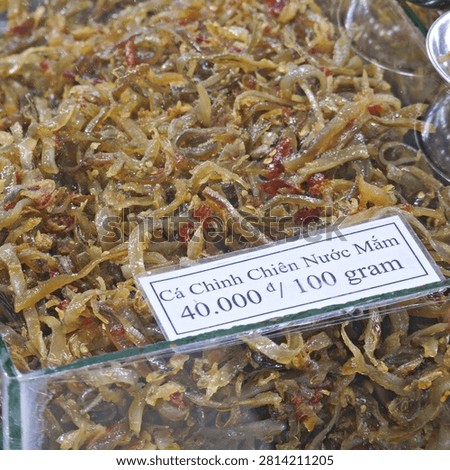 Close-up of crispy fried eel strips seasoned with savory fish sauce and chili at a bustling market fair in Vietnam.