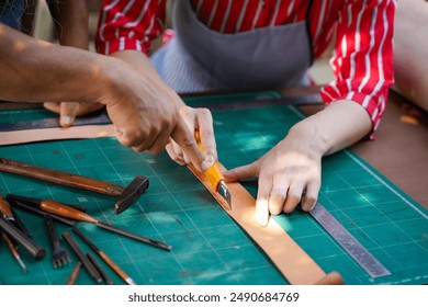 Closeup and crop hand of senior craftsman teaching young female leather maker using cutter knife cut a leathers to make belts in her workshop. - Powered by Shutterstock