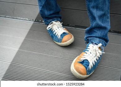 Closeup Crop Shot Of A Young Teenager Boy's Legs, He's Wearing Jeans With Sneakers Sitting Alone On An Outdoor Bench Feeling Tired Or Depressed. Teen Self-esteem, Body Image, Identity, Adolescence.