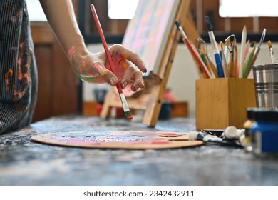 Close-up and cropped image of a young creative artist's hands smeared with watercolors holding a paintbrush to paint on a palette. - Powered by Shutterstock