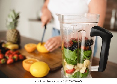 Closeup cropped photo of caucasian young woman cooking healthy smoothie drink for slimming shaping losing weight, cutting fruits vegetables for blender at home kitchen - Powered by Shutterstock