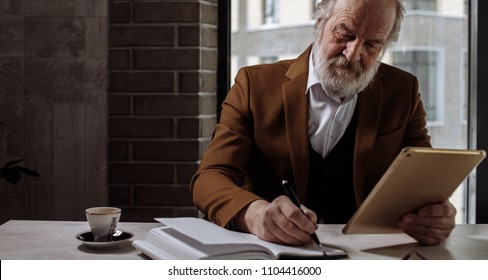 closeup cropped photo of old man rewriting information from the tablet to notebook. copy space