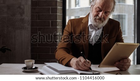 closeup cropped photo of old man rewriting information from the tablet to notebook. copy space
