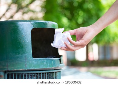 Closeup Cropped Portrait Of Someone Tossing Crumpled Piece Of Paper In Trash Can, Isolated Outdoors Green Trees Background