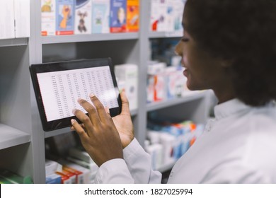 Close-up cropped shot of African American woman doctor or clinical pharmacist using digital tablet while standing in interior of modern hospital pharmacy, making drug quality control - Powered by Shutterstock