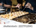 closeup cropped shot hands of chef using two takoyaki picks to turn octopus dumpling balls on pan at a food stall in Shinsekai area in Osaka Japan