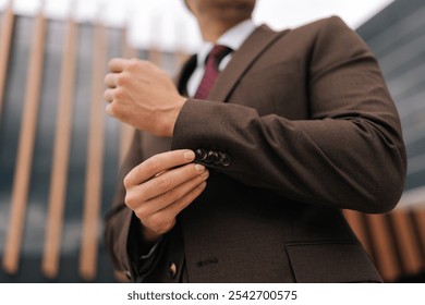 Close-up cropped shot of unrecognizable confident businessman adjusting suit button in city with modern architecture backdrop. Closeup low-angle view of business man adjusting suit outside. - Powered by Shutterstock