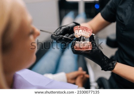 Close-up cropped shot of unrecognizable orthodontist in rubber gloves showing artificial human jaws with dental braces for teeth correction to female patient, visiting doctor orthodontic issues. ストックフォト © 