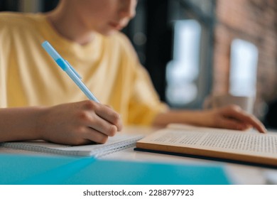 Close-up cropped shot of unrecognizable pupil boy studying at home writing in exercise book doing homework, learning sitting at table. Selective focus of schoolboy doing homework, reading textbook. - Powered by Shutterstock