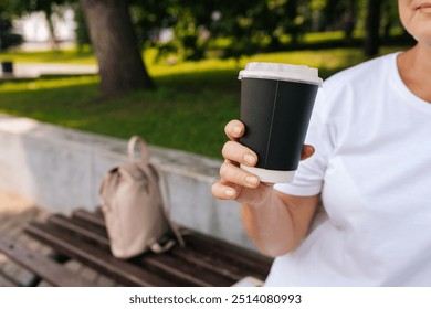 Close-up cropped shot of unrecognizable woman enjoying free time outdoors sipping coffee sitting on bench at city park. Happy female resting alone enjoying summertime. Calm lady drinking tea. - Powered by Shutterstock