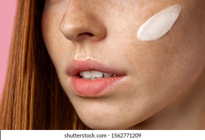 Closeup Cropped Shot Of Young Caucasian Redhead Woman With Freckles Applying Face Primer Or Moisturizing, Nourishing Cream On Her Face. Beauty Product, Cosmetic, Skin Care.