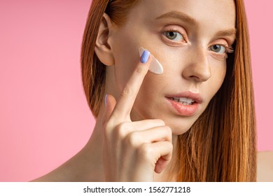 Closeup Cropped Shot Of Young Caucasian Redhead Woman Applying Foundation, Face Primer Or Moisturizer On Her Face. Beauty Product, Cosmetic, Skin Care.