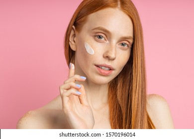 Closeup Cropped Shot Of Young Caucasian Redhead Woman Applying Foundation, Face Primer Or Moisturizer On Her Face. Beauty Product, Cosmetic, Skin Care.