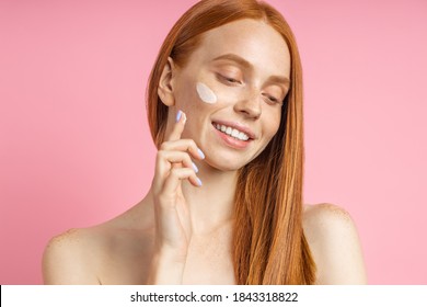 Closeup Cropped Shot Of Young Caucasian Redhead Woman Applying Foundation, Face Primer Or Moisturizer On Her Face. Beauty Product, Cosmetic, Skin Care.