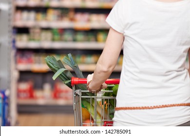 Closeup Cropped View From Behind Of A Woman Shopping In A Supermarket Pushing A Trolley Full Of Fresh Produce