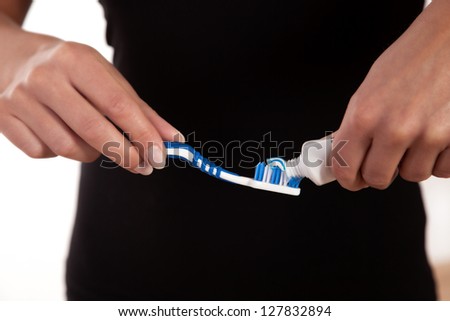 Closeup cropped view of a womans torso and hands as she sqeezes toothpaste onto a toothbrush