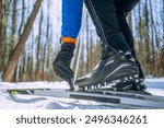 Close-up of cross-country skier fastening boots to skis, preparing for a winter adventure in a snowy forest. Sports training in the forest on a ski track, skiing.