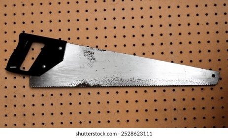 closeup of crosscut hand saw hanging on a pegboard wall