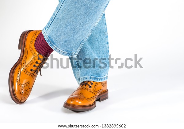 Closeup\
of Crossed Mens Legs in Brown Oxford Brogue Shoes. Posing in Blue\
Jeans Against White Background. Horizontal\
Image