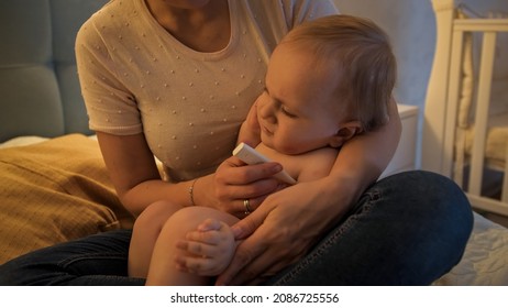 Closeup Of Crying Sick Baby Boy Sitting On Mothers' Lap And Measuring Body Temperature.