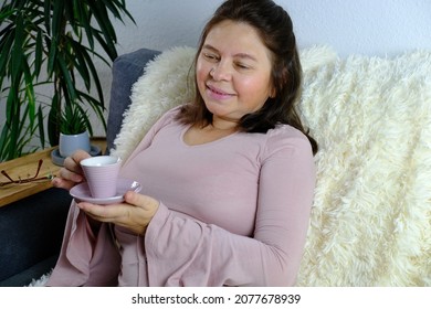 Close-up Of Cup Of Coffee, Tea, Middle-aged Woman Of 50 Years Old In Pink Sweater Sits On Sofa In Room, Concept Of Technology, Stay At Home , Cozy Home