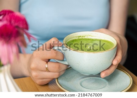 Close-up, a cup with green matcha drink in female hands.