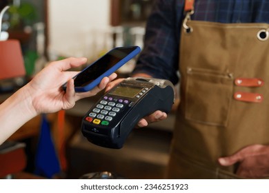 Close-up customer hand is using smartphone to scan QR code from credit card reader to pay for coffee and bakery. Minimize contact and don't use cash to pay. In a cafe while traveling - Powered by Shutterstock