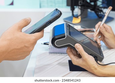 Close-up of a customer holding his smartphone paying using nfc technology, card reader machine for the customer to make the payment transaction with the contactless method. . High quality photo
