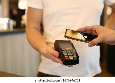 Close-up of customer person making payment via terminal and mobile phone in cafe. Pay by smartphone. Contactless nfc and modern device technology concept