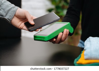 Close-up of customer person making payment via nfc terminal and mobile phone in clothes shop. Pay with smartphone. Contactless nfc and modern device technology concept - Shutterstock ID 1778037227