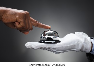 Close-up Of Customer Ringing Service Bell Held By Butler In Front Of Grey Background