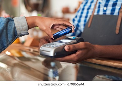 Closeup of a customer using her credit card and nfs technology to pay a barista for her purchase at a cafe - Powered by Shutterstock