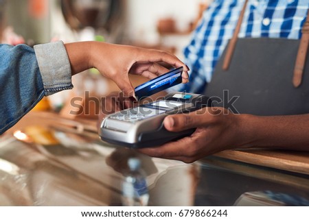 Closeup of a customer using her credit card and nfs technology to pay a barista for her purchase at a cafe