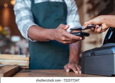 Closeup of a customer using her smartphone and nfs technology to pay a barista for her purchase at a cafe