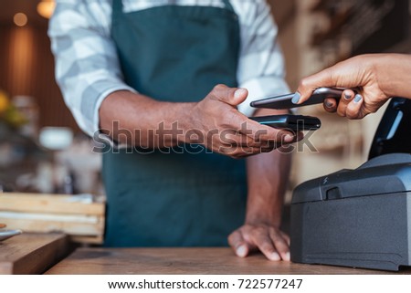 Closeup of a customer using her smartphone and nfs technology to pay a barista for her purchase at a cafe
