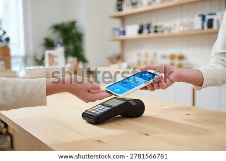 Close-up of a customer using a smartphone to make a contactless payment at a retail store's point of sale terminal.