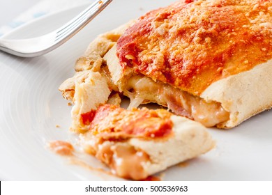 Close-up Of A Cut Open Calzone, A Type Of Folded Pizza, Showing The Melted Oozing Cheese On A White Plate