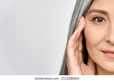 Closeup cut portrait of happy middle aged mature asian woman, senior older 50 year lady looking at camera touching her face isolated on white. Ads of eye lifting anti wrinkle skin care cream.