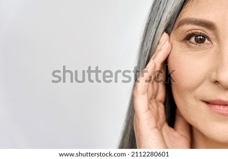 Closeup cut portrait of happy middle aged mature asian woman, senior older 50 year lady looking at camera touching her face isolated on white. Ads of eye lifting anti wrinkle skin care cream.