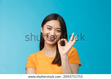 Close-up cute asian friendly girl supports your fantastic idea, smiling broadly, show okay ok sign approval, accept terms, agree take part event, stand blue background satisfied, judging nice work