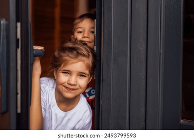 Close-up of cute children peeking out of the doorway. Little brother and sister open the front door. Cute kids meet their parents or guests. A boy and a girl have fun together at home. - Powered by Shutterstock