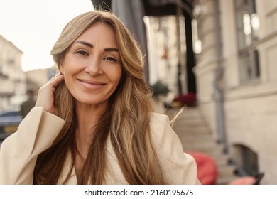 Close-up of cute fair-skinned adult woman styling blond hair behind her ear. Beauty smiles and looks into camera. Lifestyle concept of sincere emotions of people.
