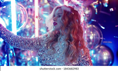 Closeup cute girl sending kiss on phone camera in nightclub. Portrait of sweet woman posing on neon lights background. Pretty girl making video on phone at night club party.