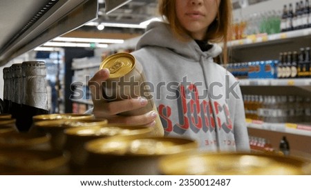 Close-up of a cute girls hand taking a golden can of beer in a supermarket