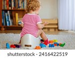 Closeup of cute little 12 months old toddler baby girl child sitting on potty. Kid playing with doll toy. Toilet training concept. Baby learning, development steps