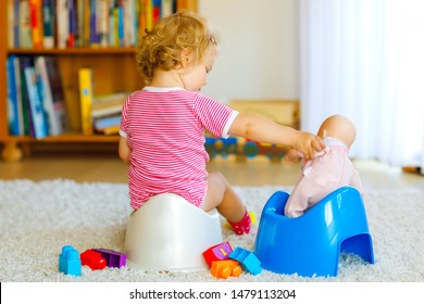 Closeup Of Cute Little 12 Months Old Toddler Baby Girl Child Sitting On Potty. Kid Playing With Doll Toy. Toilet Training Concept. Baby Learning, Development Steps