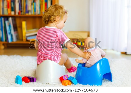 Closeup of cute little 12 months old toddler baby girl child sitting on potty. Kid playing with doll toy. Toilet training concept. Baby learning, development steps